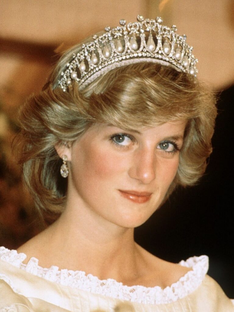 Princess Diana, a woman with coiffed blonde hair, wears an intricate diamond and pearl tiara at a banquet. One of the more intricately designed British royal tiaras.