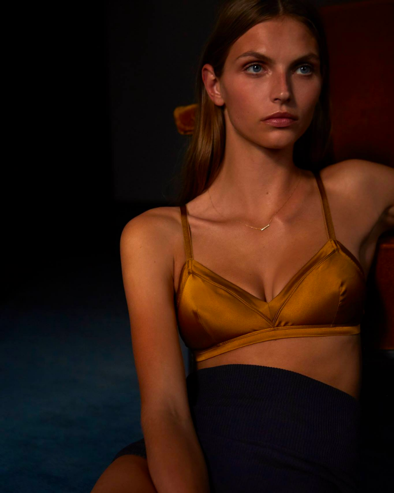 A woman in a dark room wearing a gold satin bralette and black high waisted briefs